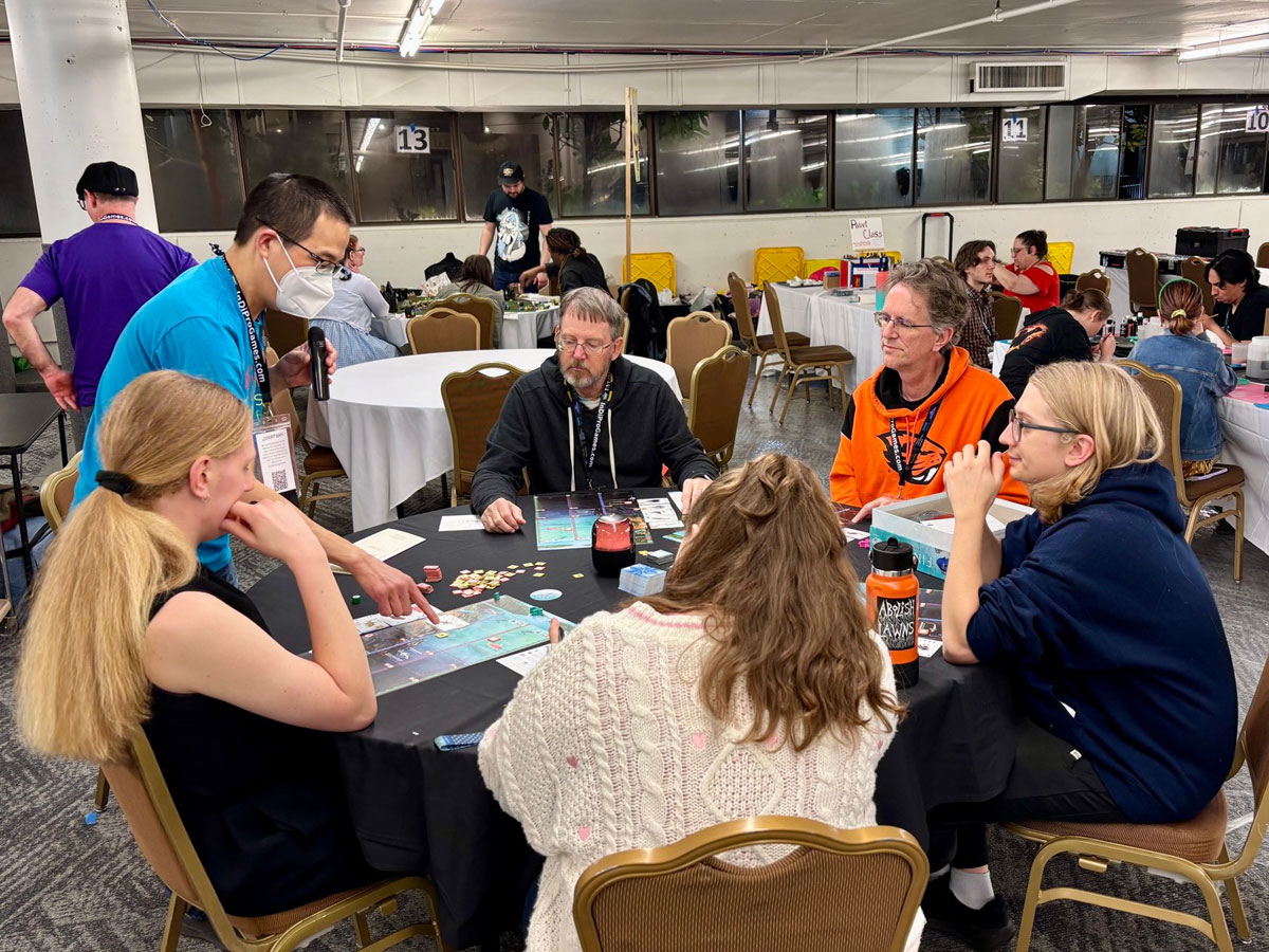 Jonathan standing and teaching Finspan to five players around a round table at GameStorm 25. Photo: Michael O'Connell
